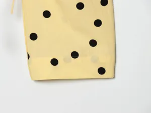 Close-up detail of yellow and black polka dot fabric garment cuff with drawstring.