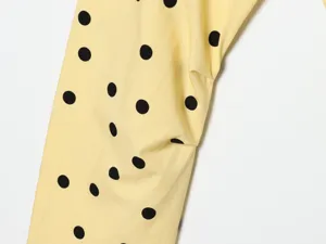 Close up detail of yellow fabric with black polka dots and pleats texture for women apparel.
