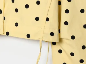 Close-up detail of a yellow and black polka dot women's long sleeve jacket with drawstrings.