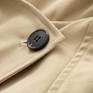 Detailed close-up shot of women's trench coat fabric, showing the stylish button and lapel stitching.