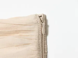 Close-up detail view of elegant beige pleated fabric apparel featuring a neat zipper closure.