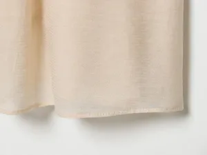 Close-up view of lightweight textured fabric hemline, fine stitching detail, elegant light beige tone.