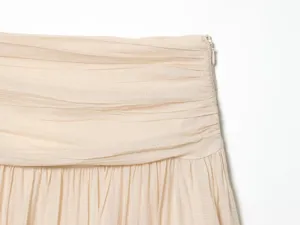 Beige pleated garment detail view showing fine texture and side zipper craftsmanship.