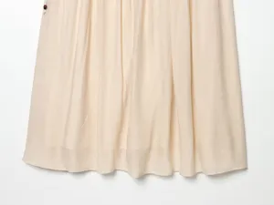Close-up detail of pleated fabric skirt in beige, soft textured material with side button.