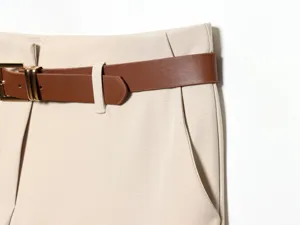 Gros plan détail de pantalon décontracté taille haute pour femme avec ceinture cuir et boucle métal.