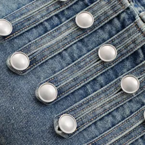 Close-up view of distressed denim fabric featuring metallic dome buttons and straps.