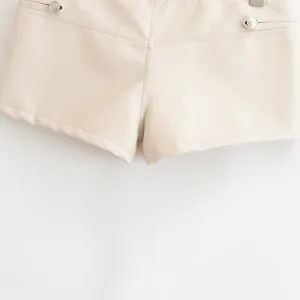 Gros plan de short en similicuir blanc cassé avec boutons métalliques et belles finitions.