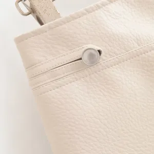 Gros plan veste similicuir blanc cassé texture grainée, bouton métallique et coutures soignées.