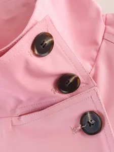 Close-up detail of women pink trench coat featuring classic double-breasted buttons and pocket.