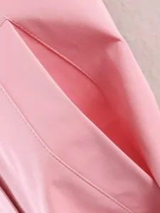 Close-up detail of stylish pink trench coat fabric, showing neat stitching and pocket.