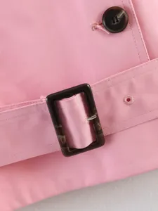 Detailed close-up of women pink trench coat featuring classic tortoise shell buckle belt.