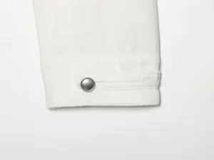 Detail der weissen Jeansjacken Aermel mit klassischem Metallknopf und Manschettenlasche.