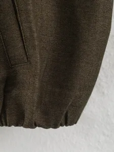 Dark brown jacket fabric detail, showing texture, elastic hem and pocket design.