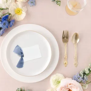 Elegante juego de tarjetas de sitio de boda con cinta azul, platos blancos y cubiertos.