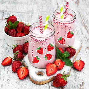 Gros plan détaillé de mignons stickers fraise sur des bocal en verre, entourés de fruits.