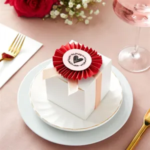 White gift box detail view featuring pink ribbon, red paper rosette flower and heart sticker.