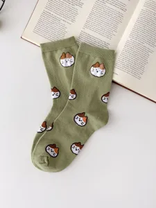 Detail shot of cute cartoon cat patterned green knit mid-calf socks laid flat on book.