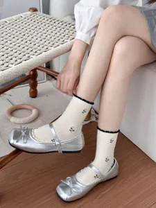 Close-up detail shot of women white floral embroidered mid-tube socks paired with silver shoes.