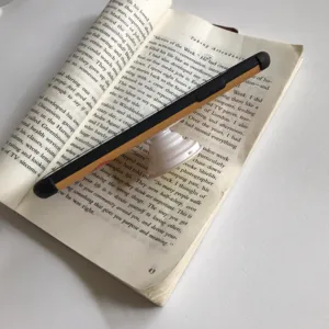 Detail view of a retractable black and yellow pop socket phone grip placed on an open book.