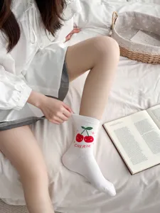 Close up of white mid-tube socks featuring cute cherry pattern and text detail. Soft cotton.