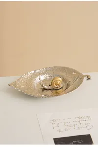 Detail shot of metal leaf incense holder with a gold snail figurine on white table.