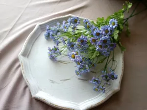 Detail view of a blue artificial chamomile bouquet displayed on a white tray, soft aesthetic.