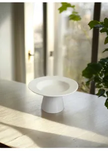 White ceramic high foot dessert plate detail, minimalist tabletop decor and fruit tray display.