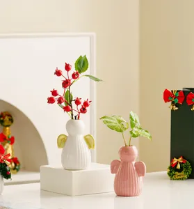 Close up of ceramic angel vases with green plants and red berries on a warm desk decor.