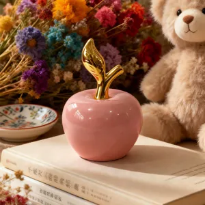 Oggetto decorativo mela in ceramica rosa con dettaglio stelo dorato su libri con fiori.