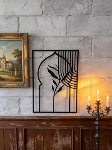Detailed view of black metal wall art with geometric arch and botanical leaves on brick wall.