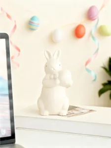 Easter ceramic bunny figurine holding egg, cute bow tie rabbit decor for home desktop.