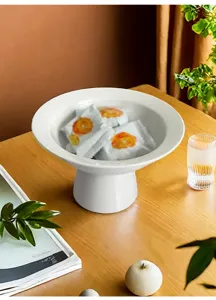 Detail view of modern minimalist white ceramic footed fruit plate placed on wooden tabletop decor.