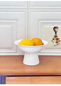 Detail shot of a modern minimalist white ceramic pedestal fruit bowl, elegant desktop dessert tray.
