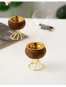 Close-up detail of modern wooden incense burner with gold metal stand and tray on table.