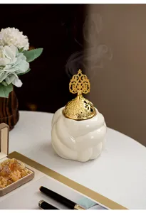 Detailed close-up of a modern ceramic incense burner with an intricate gold metal lid and smoke.