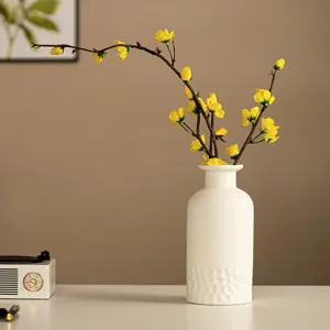 Gros plan d'un vase en céramique blanche nordique avec des fleurs artificielles jaunes vives.