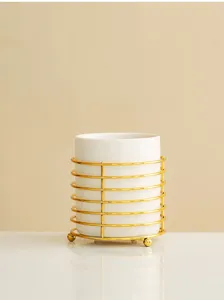 Detailed shot of white ceramic makeup brush holder with modern gold metal frame stand.