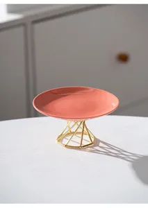 Modern pink ceramic cake stand with gold geometric metal base for dessert and fruit display.