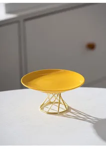Modern minimalist ceramic cake stand detail, yellow fruit plate with gold metal geometric base.