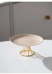 Detail shot of ceramic dessert plate with geometric gold metal stand on white table.