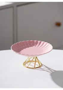 Pink ceramic cake plate with gold metal geometric high foot stand for dessert and fruit display.