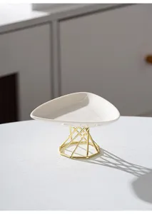 Modern minimalist ceramic cake tray detail, white triangular plate with gold geometric metal stand.