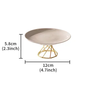 Modern minimalist ceramic cake stand with gold geometric metal base for dessert fruit display.