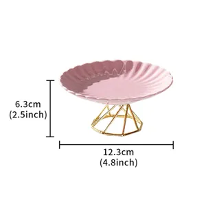 Pink ceramic cake plate detail featuring geometric gold metal stand and wavy edge.
