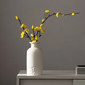 Vase en céramique blanche avec fleurs artificielles jaunes, décoration d'intérieur moderne.