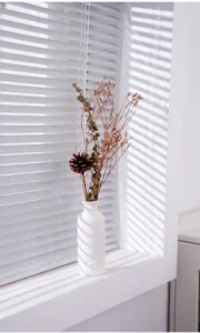Vase en céramique blanche minimaliste avec détail de fleurs séchées pour décoration.