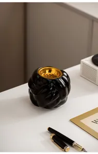 Detailansicht eines schwarzen Keramik-Raucherfasses mit goldener Innenschale am weissen Tisch.