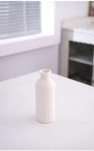 Gros plan d'un joli vase en céramique blanche minimaliste sur une table claire et lumineuse.