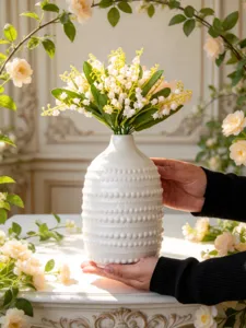 Vue détaillée d'un vase en céramique blanche avec des fleurs de muguet pour la décoration.