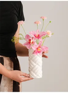 Close-up detail of a modern minimalist white ceramic braided vase with pink flowers.